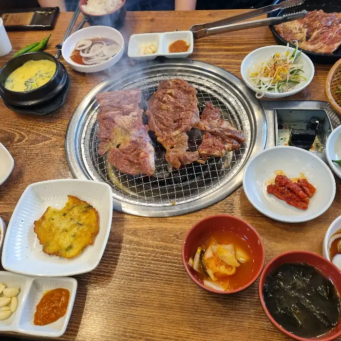 불판 위에서 지글지글 익어가는 돼지갈비와 다양한 밑반찬. 군침 도는 비주얼입니다.