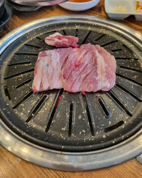 두툼한 돼지갈비 덩어리가 불판 위에서 맛있게 익어가고 있습니다.