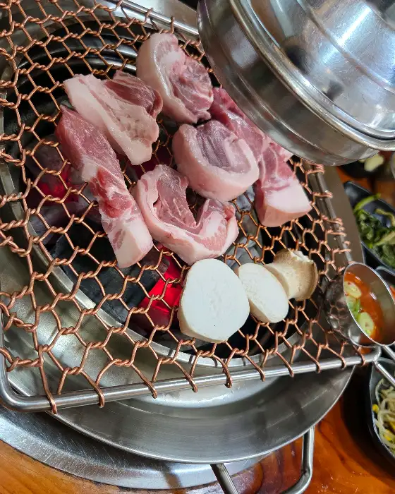 화로 위에서 노릇하게 익어가는 삼겹살과 곁들임 버섯