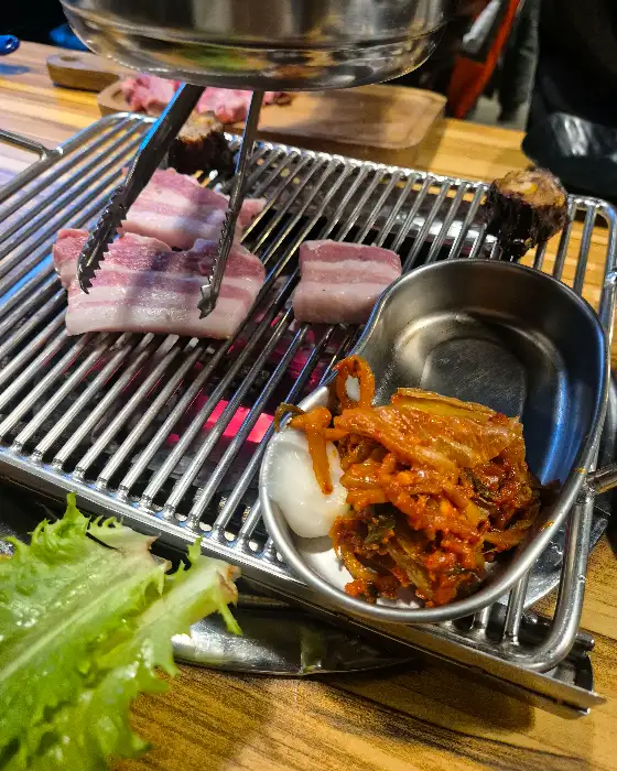 잘 익은 삼겹살 한 점을 쌈 채소와 함께 싸 먹는 모습