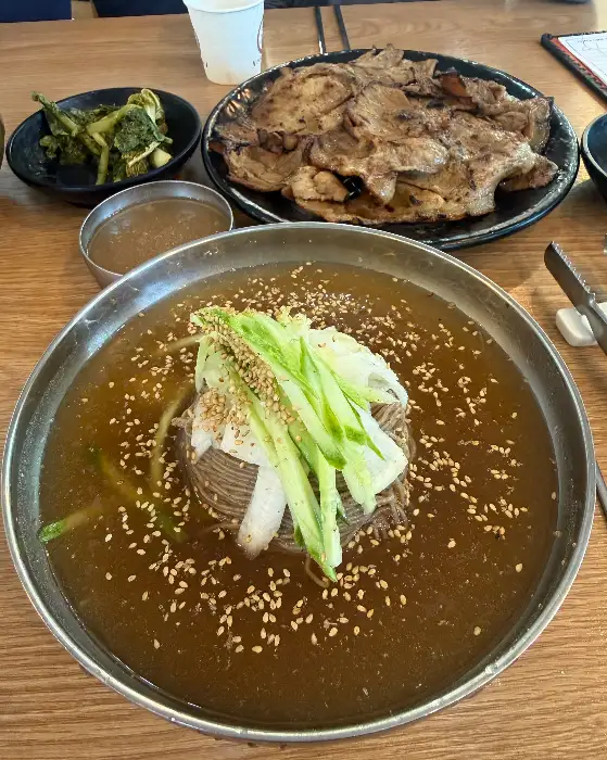 앞 접시에 덜어놓은 숯불고기와 함께 물냉면이 보입니다. 얇게 썬 고기는 숯불 향이 배어 있고, 냉면의 맑은 육수가 시원함을 더합니다.
