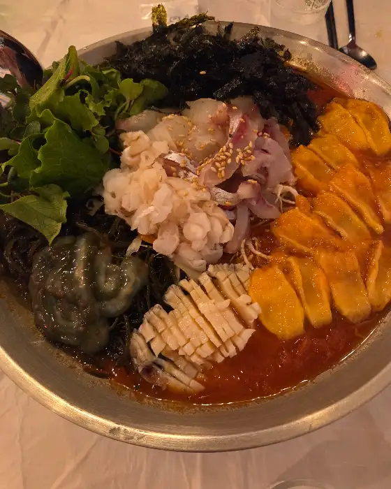막회의 근접 사진. 얇게 썰린 회 위에 참깨가 뿌려져 있고, 주변에는 쌈 채소와 다양한 곁들임 소스가 보인다.