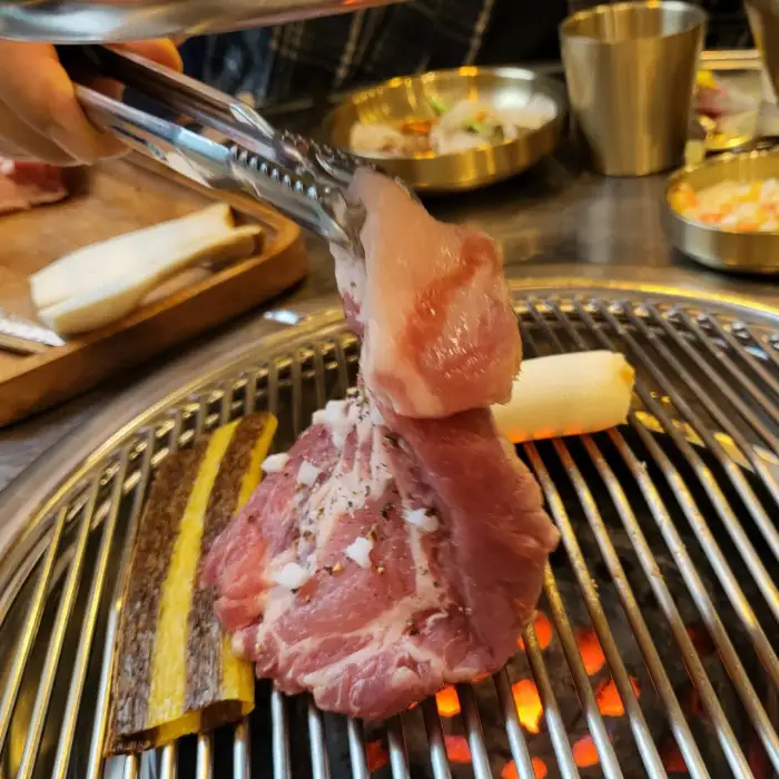 집게로 연탄불 위에서 고기를 뒤집는 모습