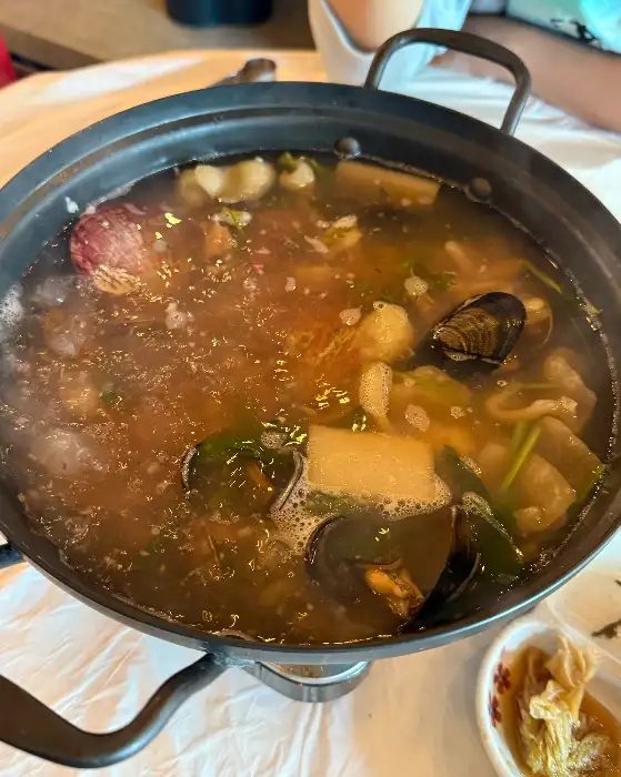 김이 모락모락 나는 냄비에 담긴 꽃게탕. 꽃게, 홍합, 조개, 채소 등이 푸짐하게 들어있으며, 붉은 국물이 먹음직스럽다.