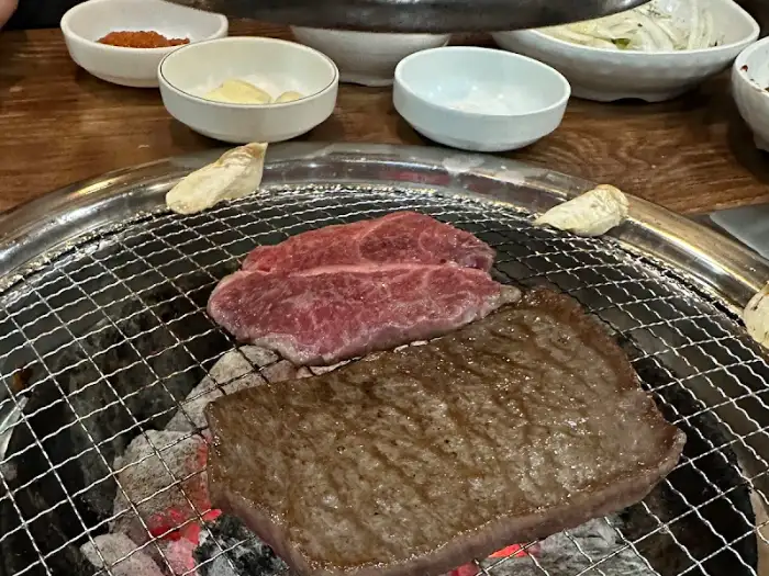 숯불 위에서 맛있게 익어가는 갈비와 꽃등심, 그리고 주변의 각종 곁들임 반찬들