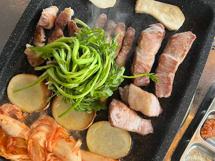 불판 위에 가지런히 놓인 고기, 김치, 감자, 버섯, 미나리