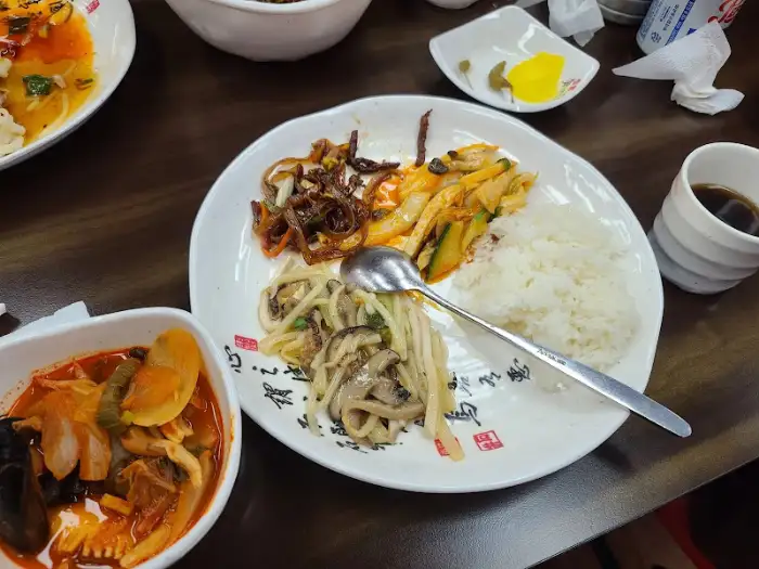 테이블 위에 놓인 다양한 중식 요리들과 밥, 그리고 젓가락과 숟가락이 놓여있는 모습. 전체적인 식사 풍경을 보여줌