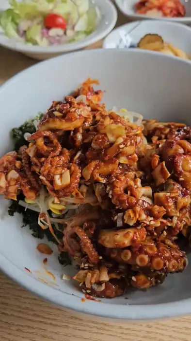 낙지비빔밥 재료가 담긴 그릇. 밥 위에 신선한 채소와 함께 매콤한 낙지볶음이 얹혀 있다.