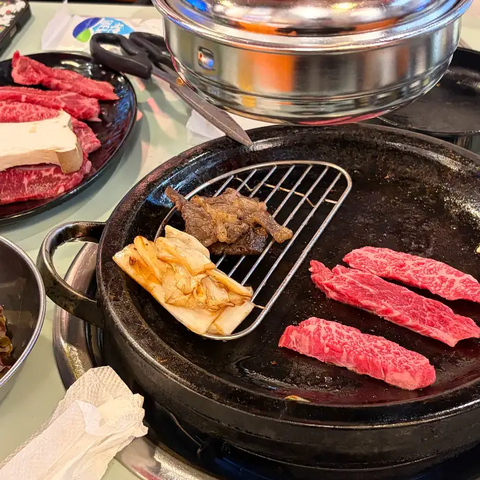 돌판 위에서 여러 종류의 고기가 구워지고 있으며, 곁들임 메뉴들도 보입니다.
