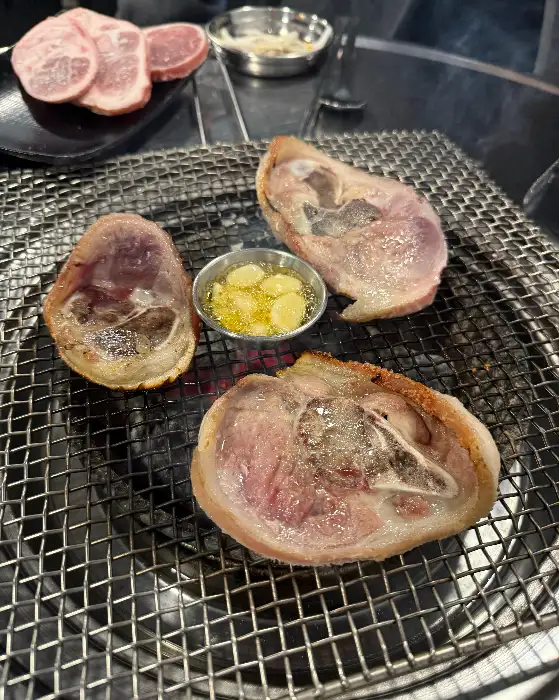 숯불 위에서 익어가는 두툼한 고기 조각과 곁들여 먹기 좋은 멜젓 같은 소스