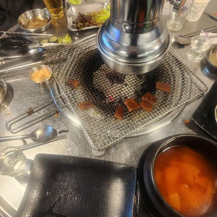 테이블에 차려진 먹음직스러운 식사 한상, 숯불 위 고기, 찌개, 밥, 김치 등