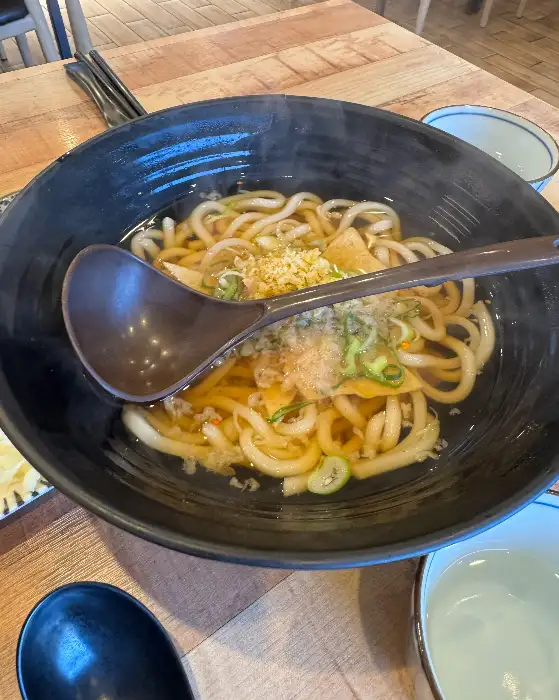 다양한 종류의 초밥이 접시에 나란히 담겨 있고, 곁들임으로 우동이 보인다