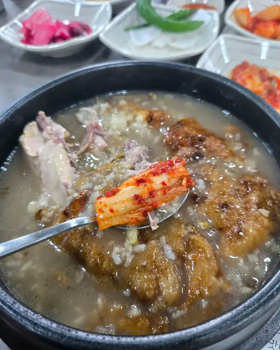 젓가락으로 집어 올린 김치와 삼계탕