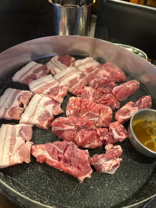 불판 위에 구워지고 있는 다양한 부위의 돼지고기