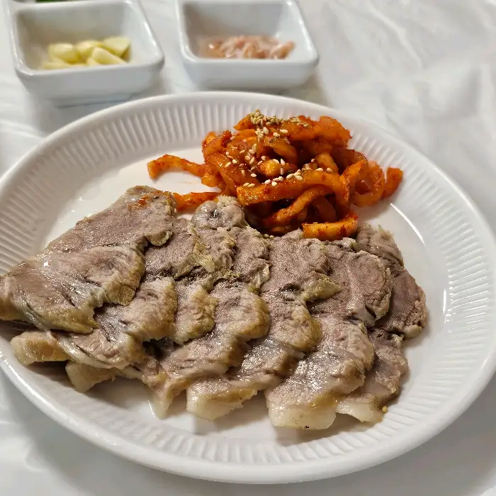 얇게 썰어 나온 수육과 빨간 양념의 무생채가 접시에 담겨 있다.