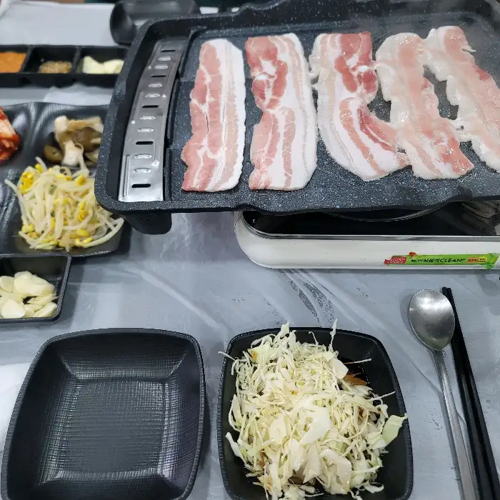 불판 위에서 구워지고 있는 삼겹살과 곁들임 찬들