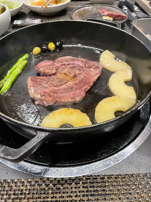 잘 구워진 한우 스테이크가 팬 위에 파인애플과 함께 놓여 있습니다.
