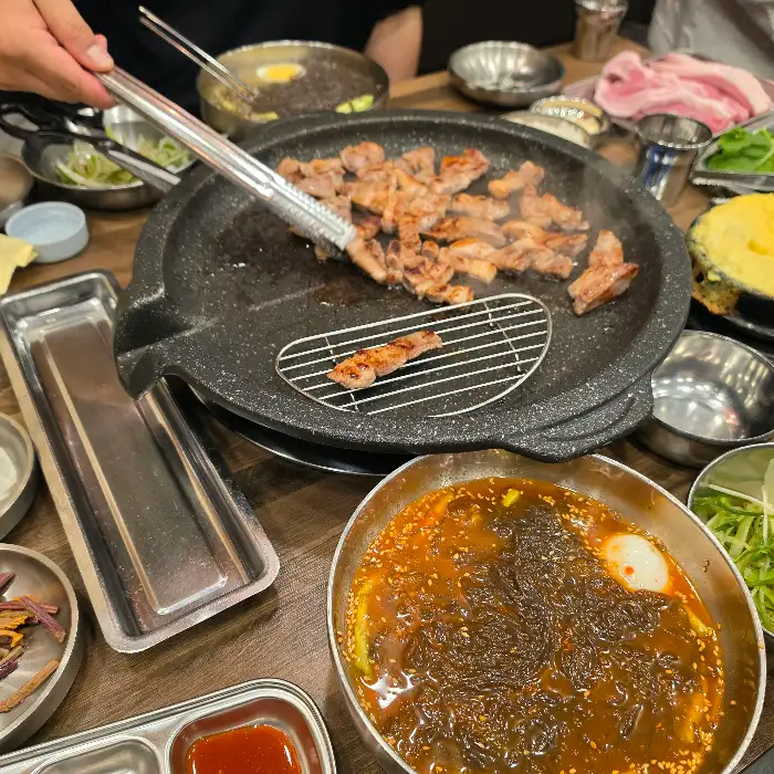불판 위에서 지글지글 익어가는 삼겹살과 곁들임 채소들