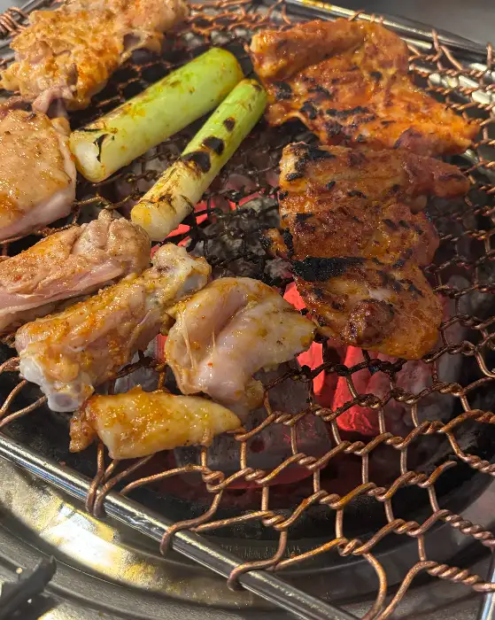 다양한 부위의 닭갈비와 구운 파가 숯불 위에서 익어가고 있는 모습
