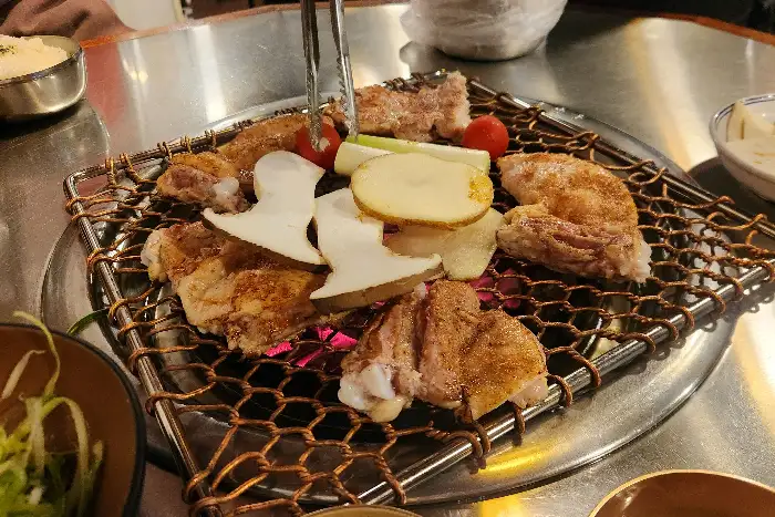 숯불 위에서 잘 익고 있는 닭갈비 조각들과 버섯, 양파, 토마토