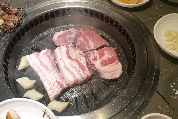 두툼한 삼겹살 덩어리가 숯불 위에서 익어가는 모습