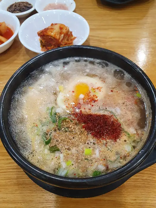 흑색 그릇에 담긴 뜨끈한 국물의 음식, 계란 노른자와 파, 고춧가루 등이 토핑되어 있는 모습