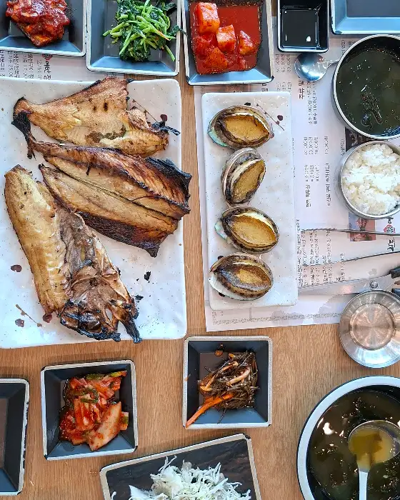 식탁 위에 놓인 생선구이, 전복구이, 밥, 국, 그리고 여러 가지 밑반찬들의 모습