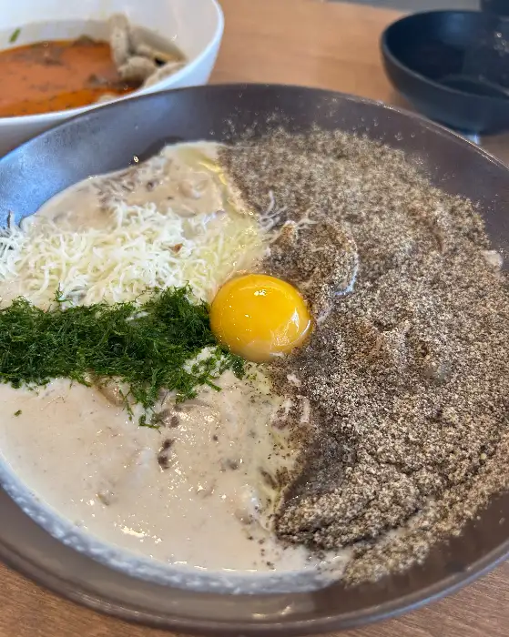 크림 수제비 위에 계란 노른자와 다진 채소가 올라가 있습니다.