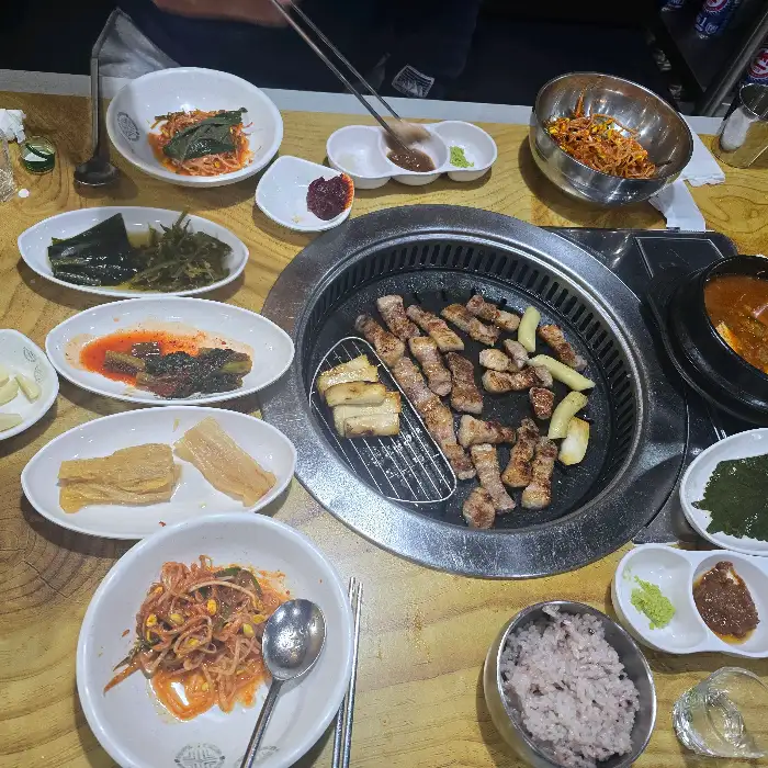 테이블 전체 모습. 불판 위에는 잘 익은 삼겹살이 있고, 다양한 밑반찬과 함께 된장찌개가 보입니다.