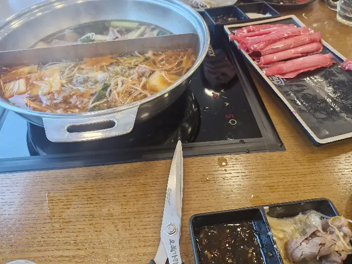 샤브샤브 냄비가 놓인 테이블에는 곁들임 메뉴로 보이는 샐러드와 소스들이 준비되어 있다.