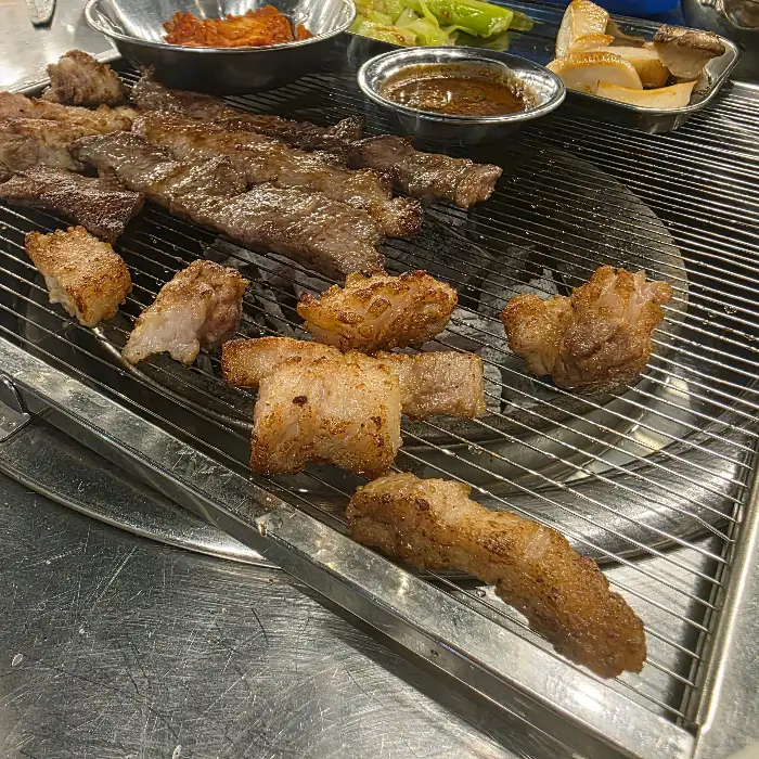 숯불 위에서 구워지고 있는 두툼한 생갈비와 다른 부위의 고기들. 노릇하게 익어 먹음직스럽다.