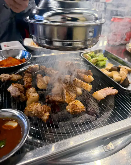 불판 위에서 지글지글 익어가고 있는 두툼한 삼겹살. 하얀 기름기가 녹아내리며 먹음직스러운 갈색으로 변하고 있다.