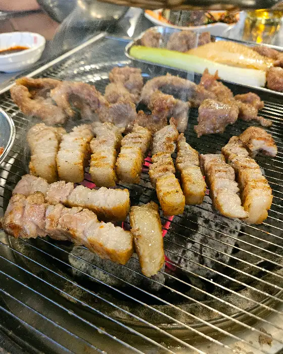 숯불 위에서 노릇하게 익고 있는 삼겹살. 지방이 잘 녹아내려 먹음직스럽다.