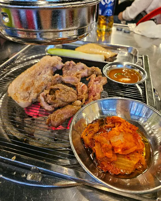 테이블 위에는 숯불 위에 구워지고 있는 고기와 함께 찍어 먹을 소스, 그리고 김치가 놓여 있다.