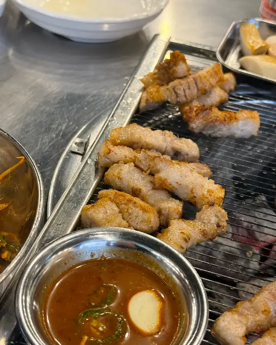 숯불 위에서 익어가는 고기와 함께 곁들여진 소스. 소스에는 다진 파와 마늘이 들어 있어 보인다.