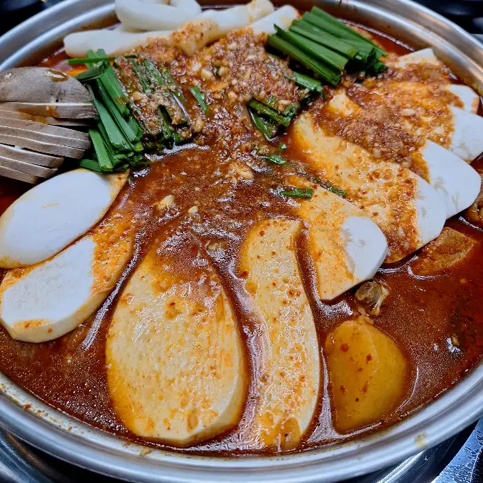닭도리탕 냄비 위에 큼직하게 썰린 버섯과 파, 떡이 얹혀져 있고, 국물이 자작하다.