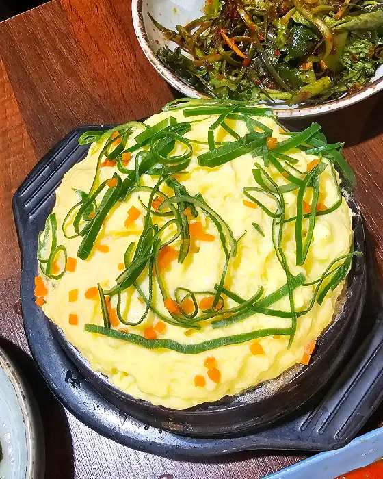 노란색 계란찜 위에 파와 당근이 올려진 모습