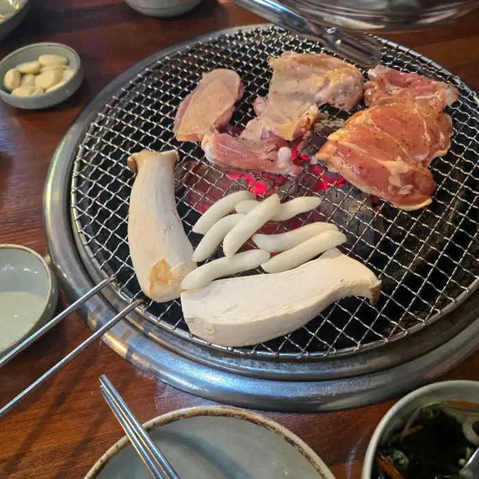 숯불 위에서 익어가는 닭갈비와 떡, 버섯, 그리고 곁들임 찬들