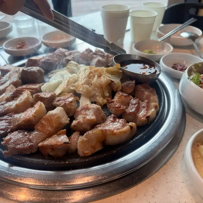 집게로 흑돼지 고기를 불판에 올리는 모습