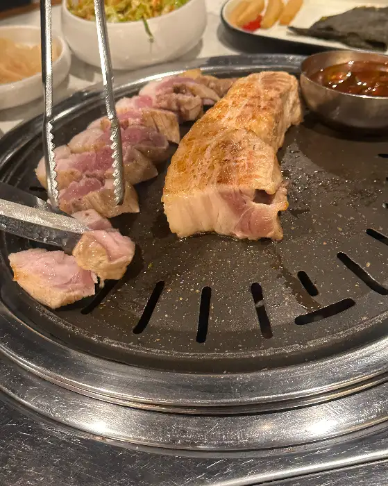 잘 구워진 흑돼지 덩어리와 집게가 불판 위에 놓여 있는 모습