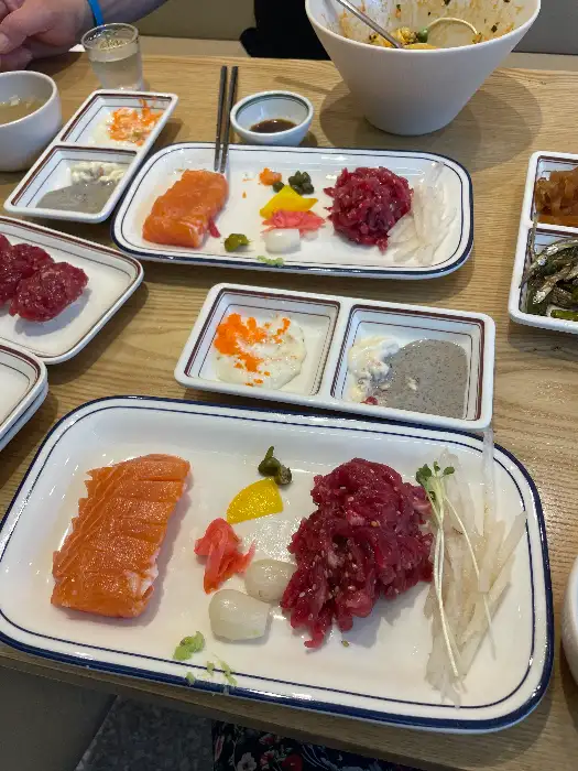 테이블에 차려진 다양한 음식들의 구성. 육회, 연어, 곁들임 찬들이 정갈하게 플레이팅되어 있다.