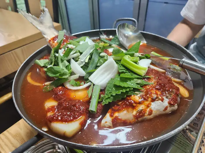 커다란 냄비에 푸짐하게 담긴 덕자 조림. 큼지막한 덕자 조각과 파, 양파가 먹음직스럽게 얹어져 있다.