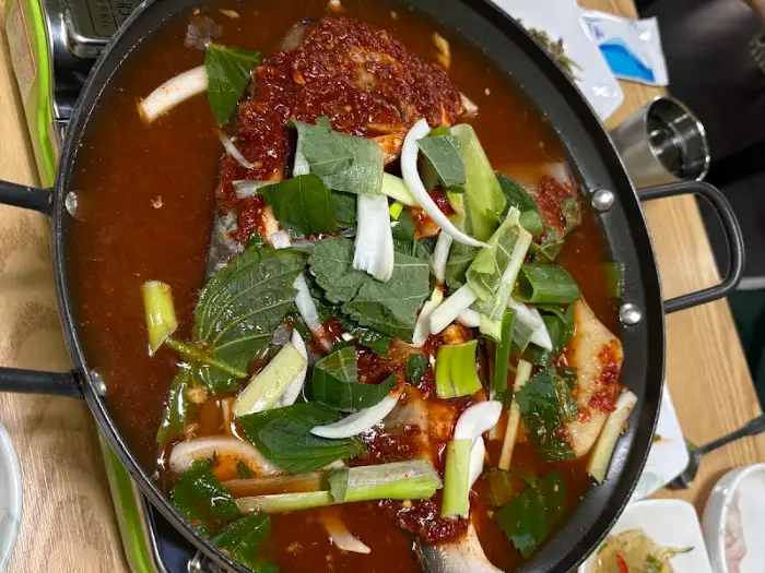 김이 모락모락 나는 덕자 조림 냄비의 위에서 찍은 사진. 붉은 양념과 채소들이 가득 담겨 있다.