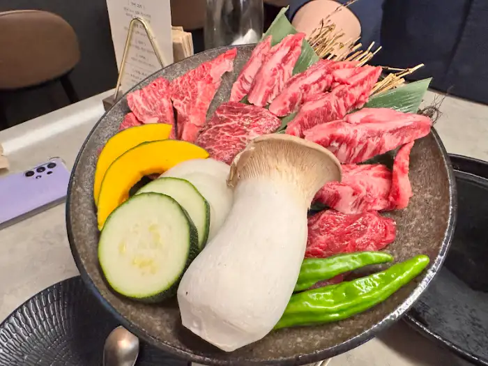 큰 접시에 신선한 소고기, 버섯, 호박, 애호박 슬라이스가 플레이팅되어 있음