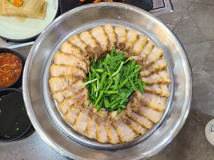 잘 익혀진 돼지고기 수육이 둥글게 펼쳐져 있고 가운데 파채가 올라간 요리
