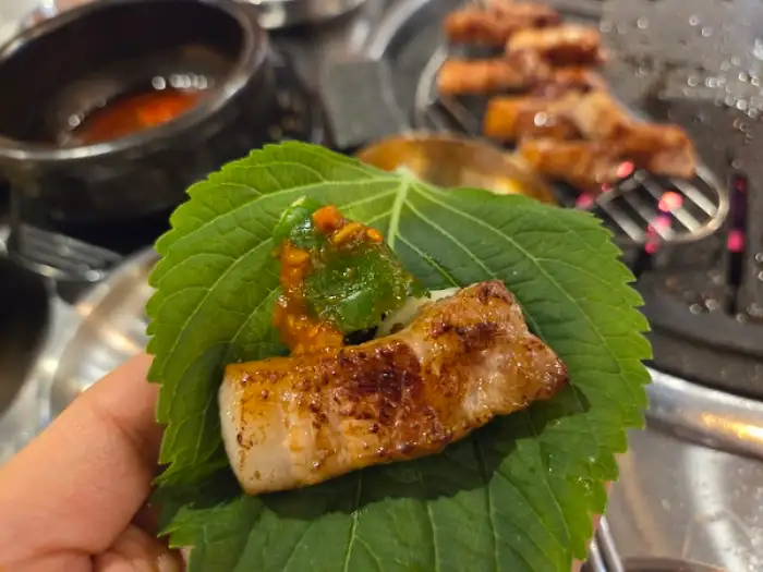 손에 쥐고 있는 쌈의 모습. 깻잎 위로 고기와 소스가 올라가 먹음직스럽다.