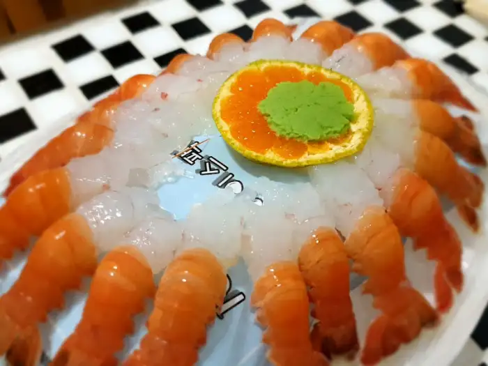 테이블에 놓인 딱새우회 접시. 신선한 딱새우가 동그랗게 배열되어 있고, 가운데에는 오렌지 조각과 와사비가 놓여 있다.