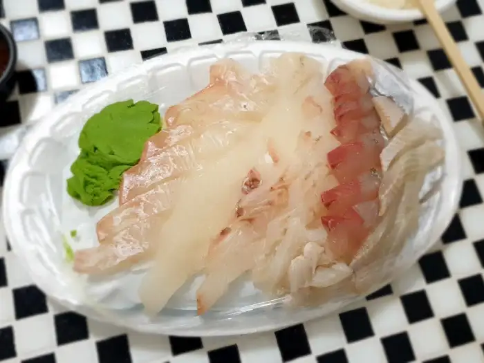 접시에 담긴 광어회. 얇게 썰린 광어회가 가지런히 놓여 있고, 옆에는 초록색 와사비가 곁들여져 있다.