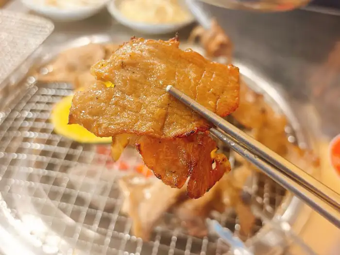 집게로 집어 올린 잘 구워진 돼지고기 한 점