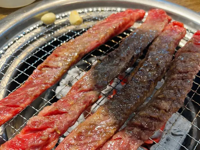 숯불 위에서 구워지고 있는 길쭉한 모양의 갈비살